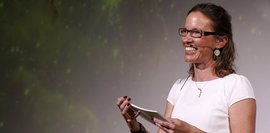 Eine Frau, die Moderationskarten in der Hand hält und in ein Publikum lacht. 