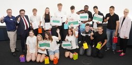 Eine Gruppe von Menschen posiert für ein Foto. Einige Personen halten Zertifikate, andere bunte Geschenktüten. 