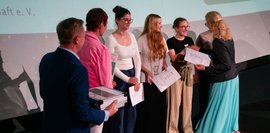 Eine Gruppe von Schülerinnen und Schülern steht auf der Bühne und nimmt von einer Frau feierlich ihre Urkunden entgegen