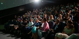 Ein Planetarium ist mit Menschen gefüllt, die in Reihen sitzen und gespannt nach vorne schauen.