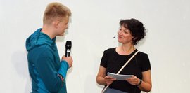 Ein Junge, der ein Mirkrofon in der Hand hält und eine Frau, die ihm gegenüber steht und zuhört.