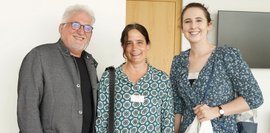 Zwei Frauen und ein Mann, die nebeneinander stehen und in die Kamera lächeln