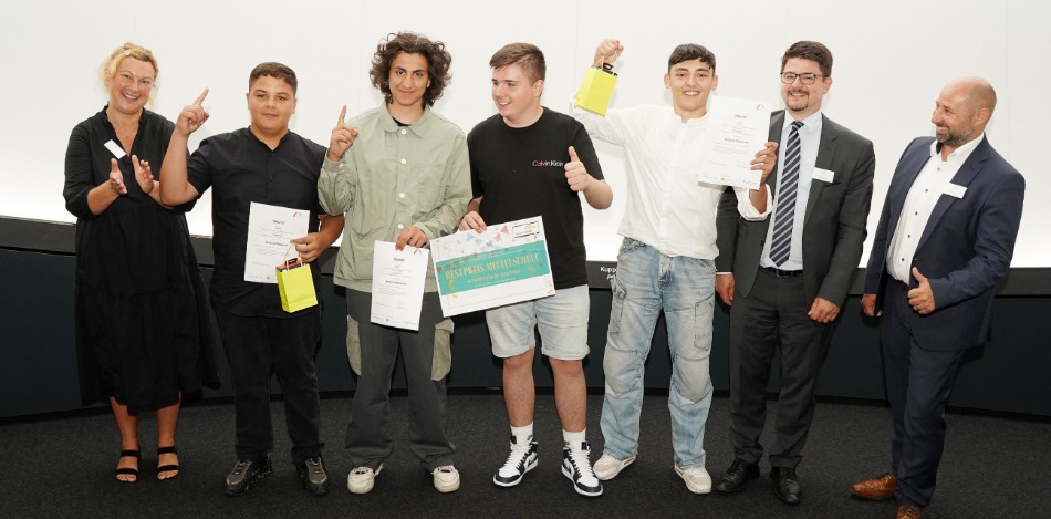 Abschlussveranstaltung 2023 Vier Schüler, die Plakate in der Hand halten und mit drei Erwachsenen jubelnd für ein Foto posieren