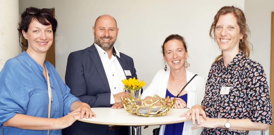 Abschlussveranstaltung 2023 Drei Frauen und ein Mann, die nebeneinander stehen und in die Kamera lächeln