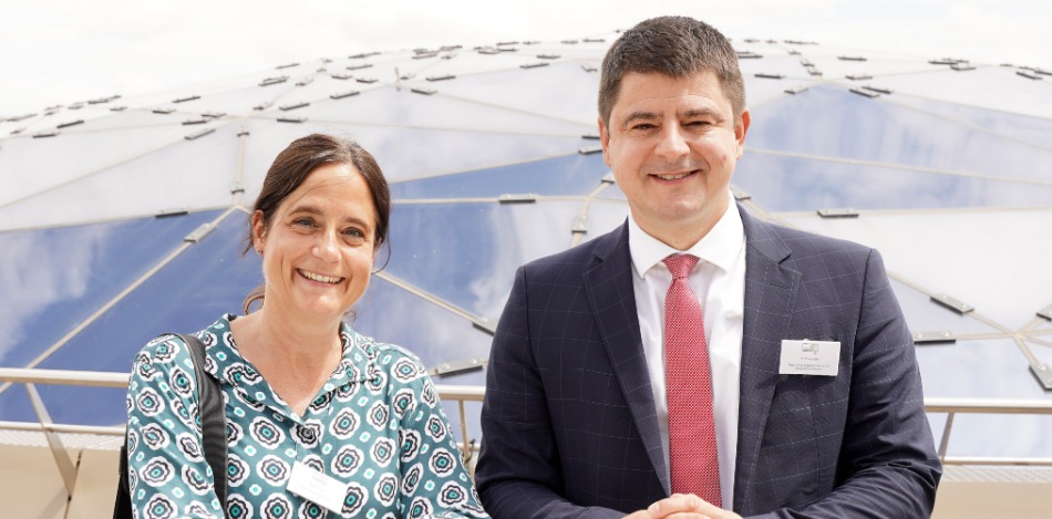 Eine Frau und ein Mann, die nebeneinander stehen und in die Kamera lächeln. 