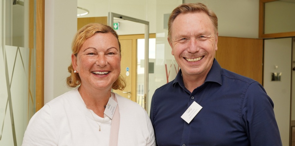 Eine Frau und ein Mann stehen nebeneinander und beide grinsen in die Kamera.