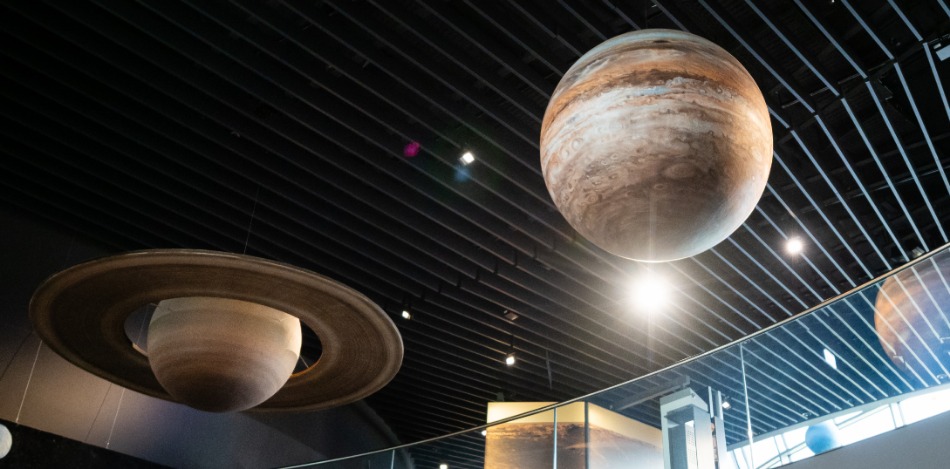 Zwei große, detailreiche Modellplaneten hängen von der Decke einer Ausstellung und schweben eindrucksvoll über dem Raum.