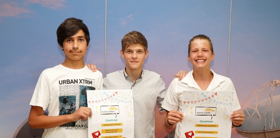 Drei Schüler, vor einer blauen Wand, die ein Plakat in der Hand halten und für ein Foto posieren