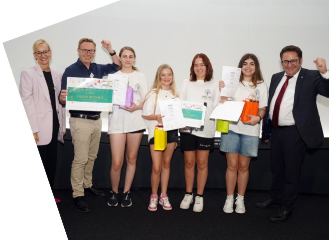 Vier Schülerinnen, die Plakate in der Hand halten und mit drei Erwachsenen für ein Foto posieren