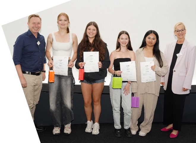 Vier Schülerinnen, die Plakate in der Hand halten und mit zwei Erwachsenen für ein Foto posieren