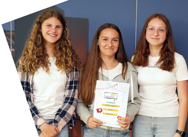 Drei Schülerinnen, vor einer blauen Wand, die für ein Foto posieren