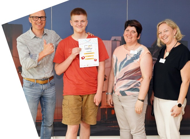 Ein Schüler, der ein Plakat in der Hand hält und mit drei Erwachsenen für ein Foto posieren