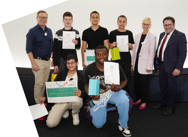 Fünf Schüler, die Plakate in der Hand halten und mit drei Erwachsenen für ein Foto posieren