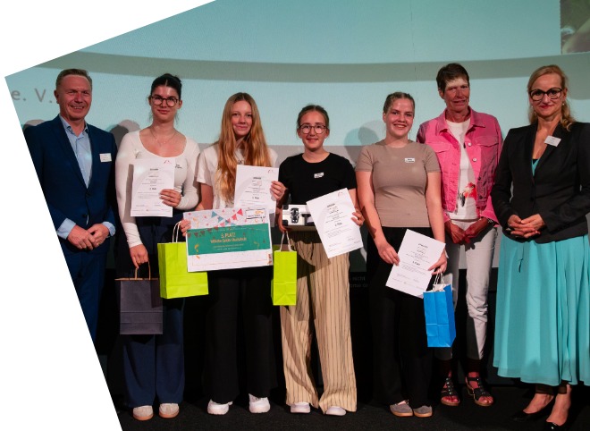 Vier Schülerinnen, die Plakate in der Hand halten und mit drei Erwachsenen für ein Foto posieren