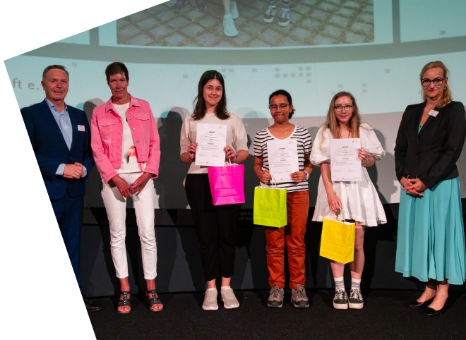 Drei Schülerinnen, die Plakate in der Hand halten und mit drei Erwachsenen für ein Foto posieren