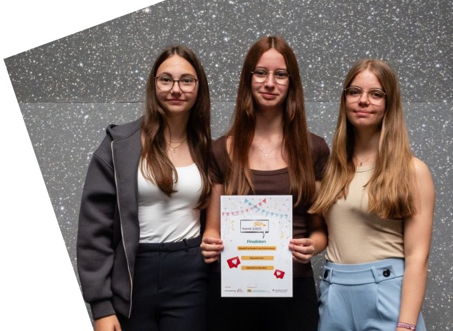 Drei Schülerinnen, die Plakate in der Hand halten und für ein Foto posieren