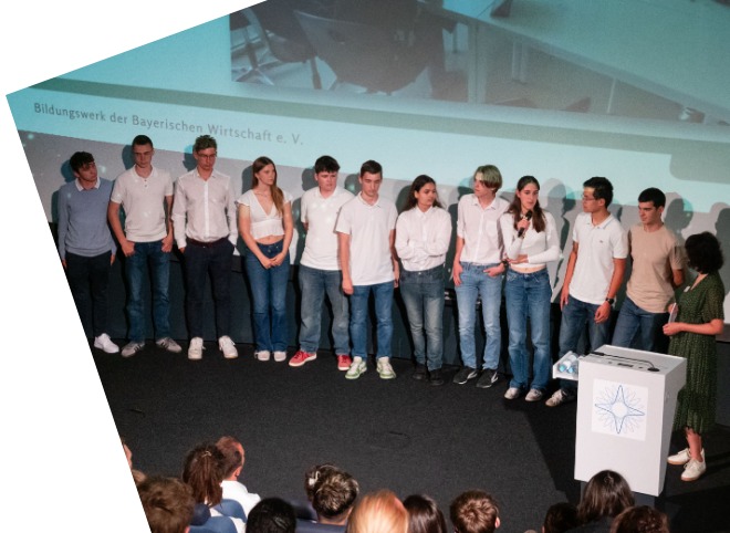 Auf dem Bild steht eine Gruppe junger Menschen auf einer Bühne und präsentiert sich vor einem Publikum.