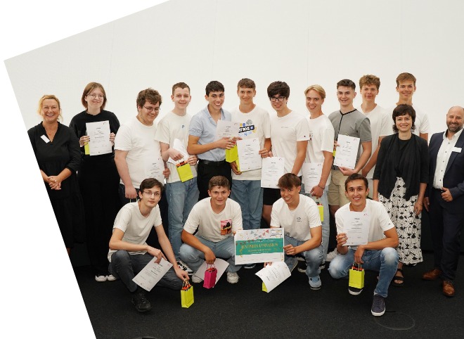 Die Gewinner des Bestpreises der Gymnasien Eine Gruppe von Schülern, die Plakate in der Hand halten und mit drei Erwachsenen für ein Foto posieren