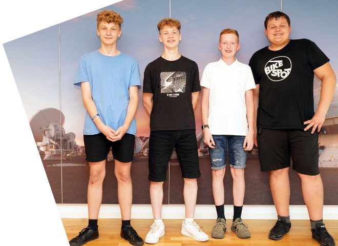Abschlussveranstaltung 2023 Vier Schüler, vor einer blauen Wand, die für ein Foto posieren