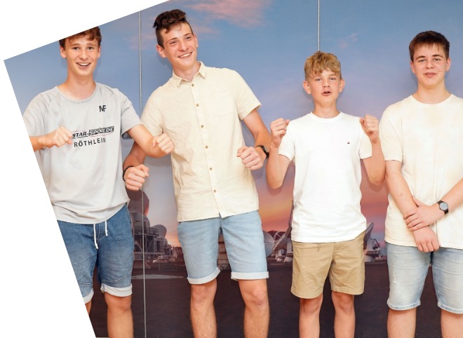 Abschlussveranstaltung 2023 Vier Schüler, vor einer blauen Wand, die für ein Foto posieren