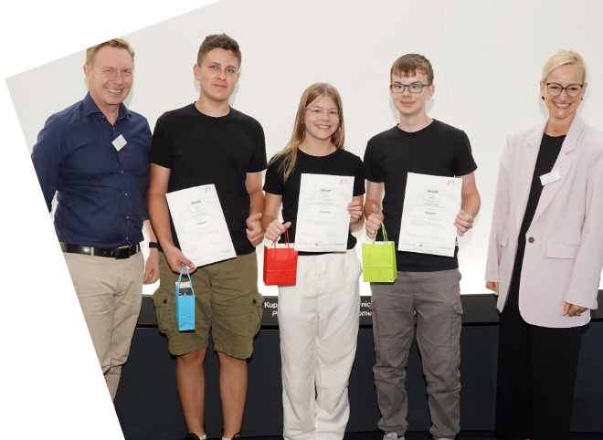 Abschlussveranstaltung 2024 Zwei Schüler und eine Schülerin, die Plakate in der Hand halten und mit zwei Erwachsenen für ein Foto posieren