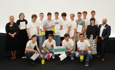 Die Gewinner des Bestpreises der Gymnasien Eine Gruppe von Schülern, die Plakate in der Hand halten und mit drei Erwachsenen für ein Foto posieren
