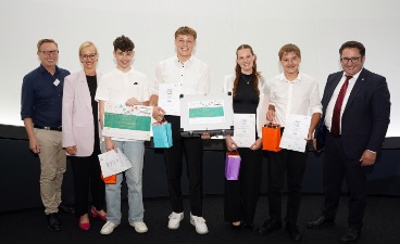 Vier Schüler, die Plakate in der Hand halten und mit drei Erwachsenen für ein Foto posieren