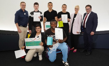 Fünf Schüler, die Plakate in der Hand halten und mit drei Erwachsenen für ein Foto posieren