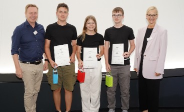 Eine Schülerin und zwei Schüler, die Plakate in der Hand halten und mit zwei Erwachsenen für ein Foto posieren