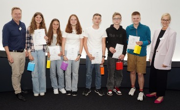 Drei Schülerinnen und drei Schüler, die Plakate in der Hand halten und mit zwei Erwachsenen für ein Foto posieren