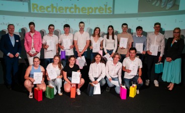 Eine Gruppe Schülerinnen und Schüler, die Plakate in der Hand halten und mit drei Erwachsenen für ein Foto posieren