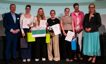 Vier Schülerinnen, die Plakate in der Hand halten und mit drei Erwachsenen für ein Foto posieren