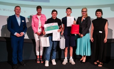 Zwei Schüler, die Plakate in der Hand halten und mit vier Erwachsenen für ein Foto posieren