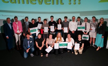 Eine Gruppe von Menschen steht auf einer Bühne und posiert für ein Gruppenfoto. Einige Personen halten Zertifikate oder Schilder in den Händen