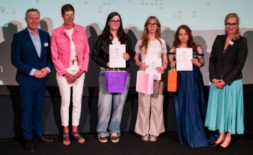 Drei Schülerinnen, die Plakate in der Hand halten und mit drei Erwachsenen für ein Foto posieren