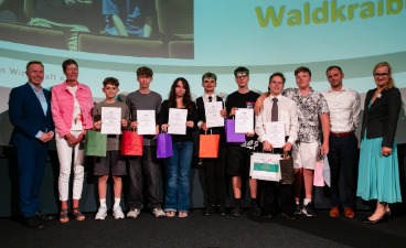 Eine Gruppe an Schülern und eine Schülerin, die Plakate in der Hand halten und mit vier Erwachsenen für ein Foto posieren